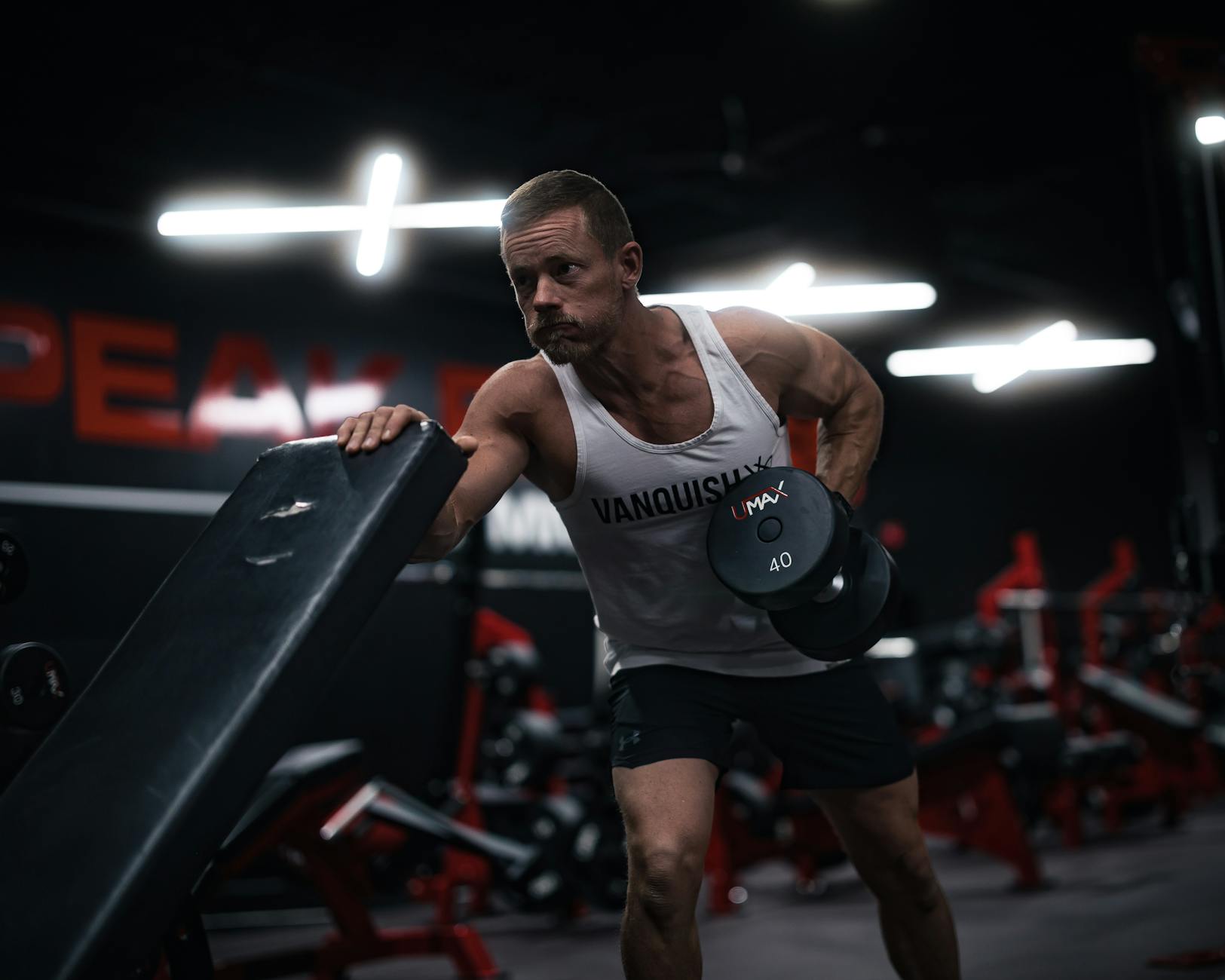 Mężczyzna po 40. roku życia wykonuje wiosłowanie hantlą na siłowni