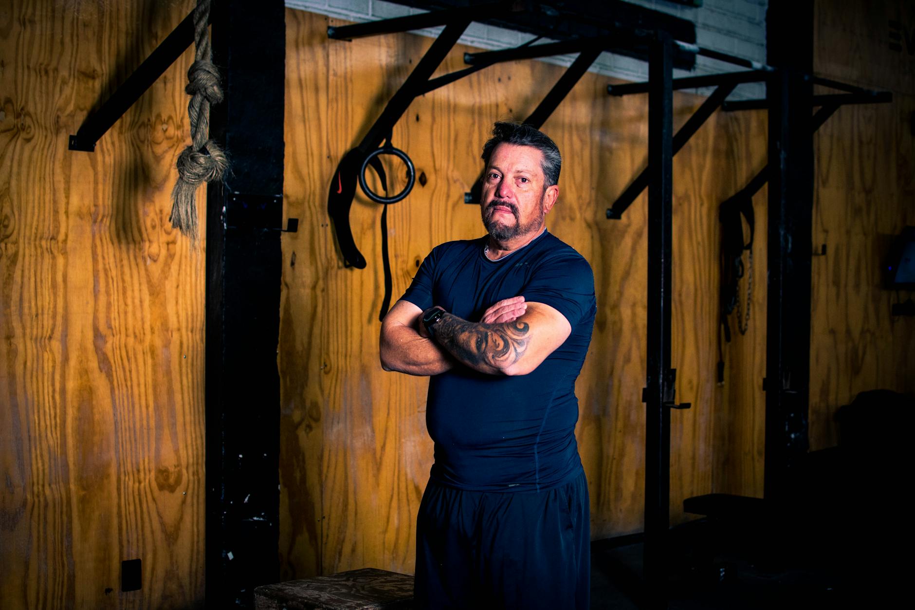 Utatuażowany mężczyzna po 40 w stroju sportowym stoi pewnie na siłowni