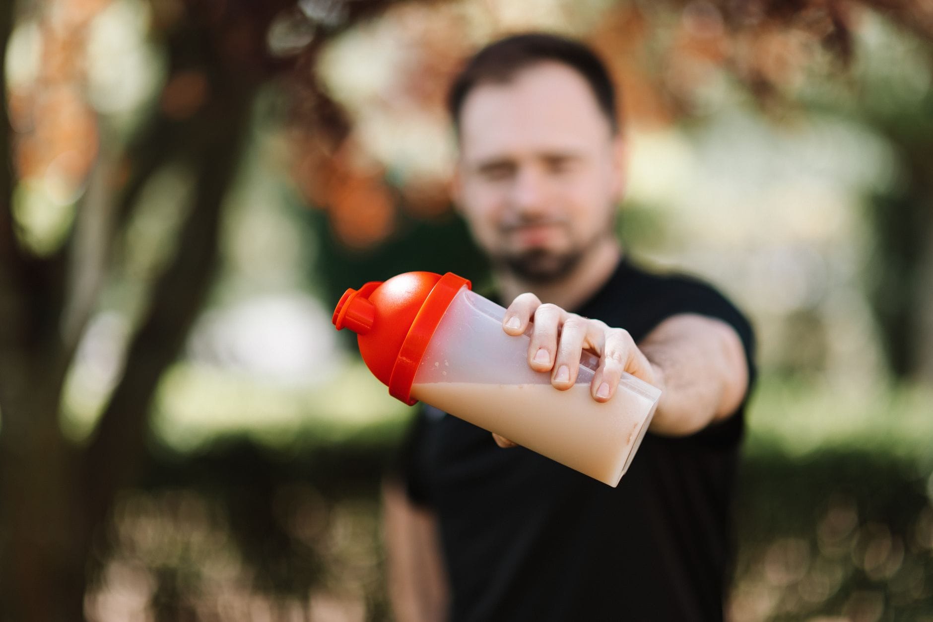 Mężczyzna trzyma shaker z przedtreningówką na tle natury